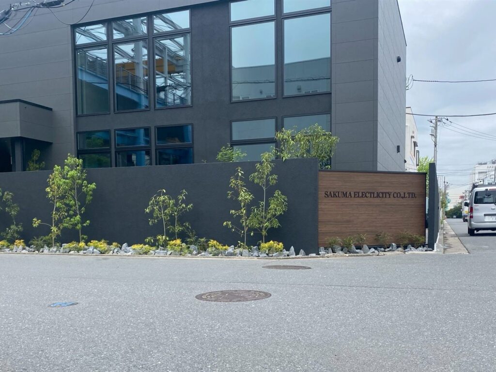 グランドアートウォール施工後。木目調サインと植栽を組み合わせたデザイン塀